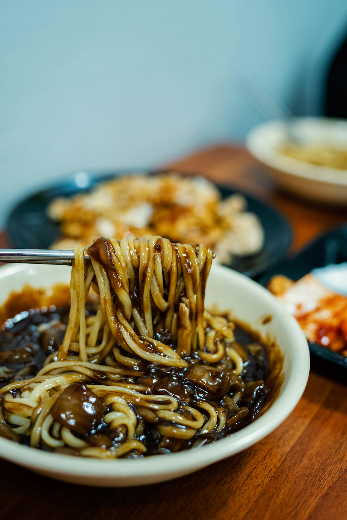 Chopsticks lifting jjajangmyeon noodles coated in black bean sauce