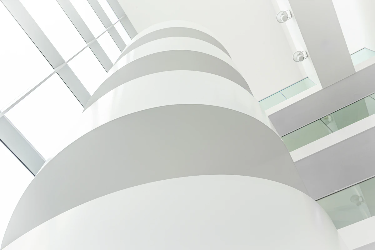 A white spiral of curving balconies inside a modern atrium, seen from below toward a glass roof