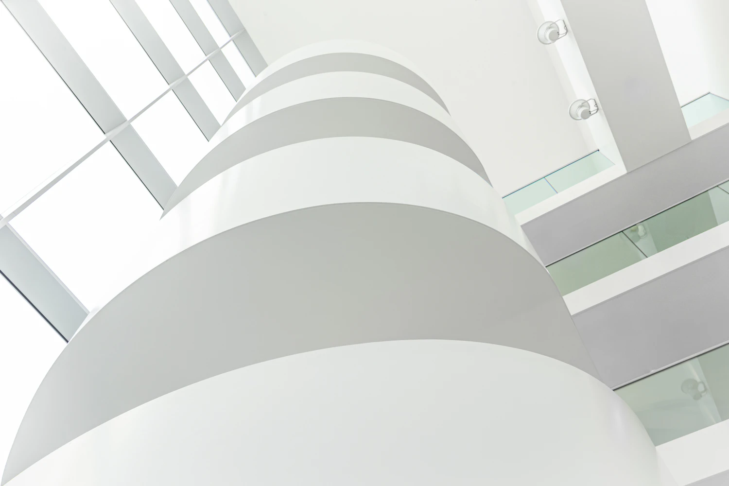 A white spiral of curving balconies inside a modern atrium, seen from below toward a glass roof
