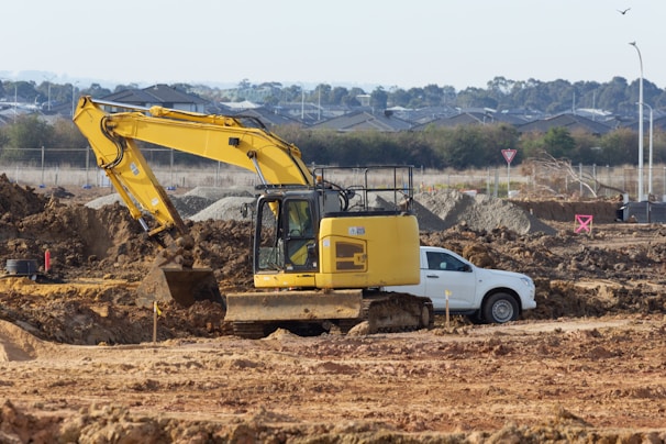 A yellow excavator is digging near a white car.