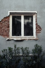 A window peeks through a damaged wall.