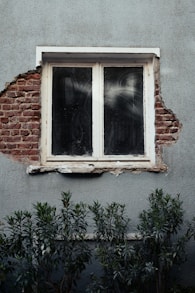 A window peeks through a damaged wall.