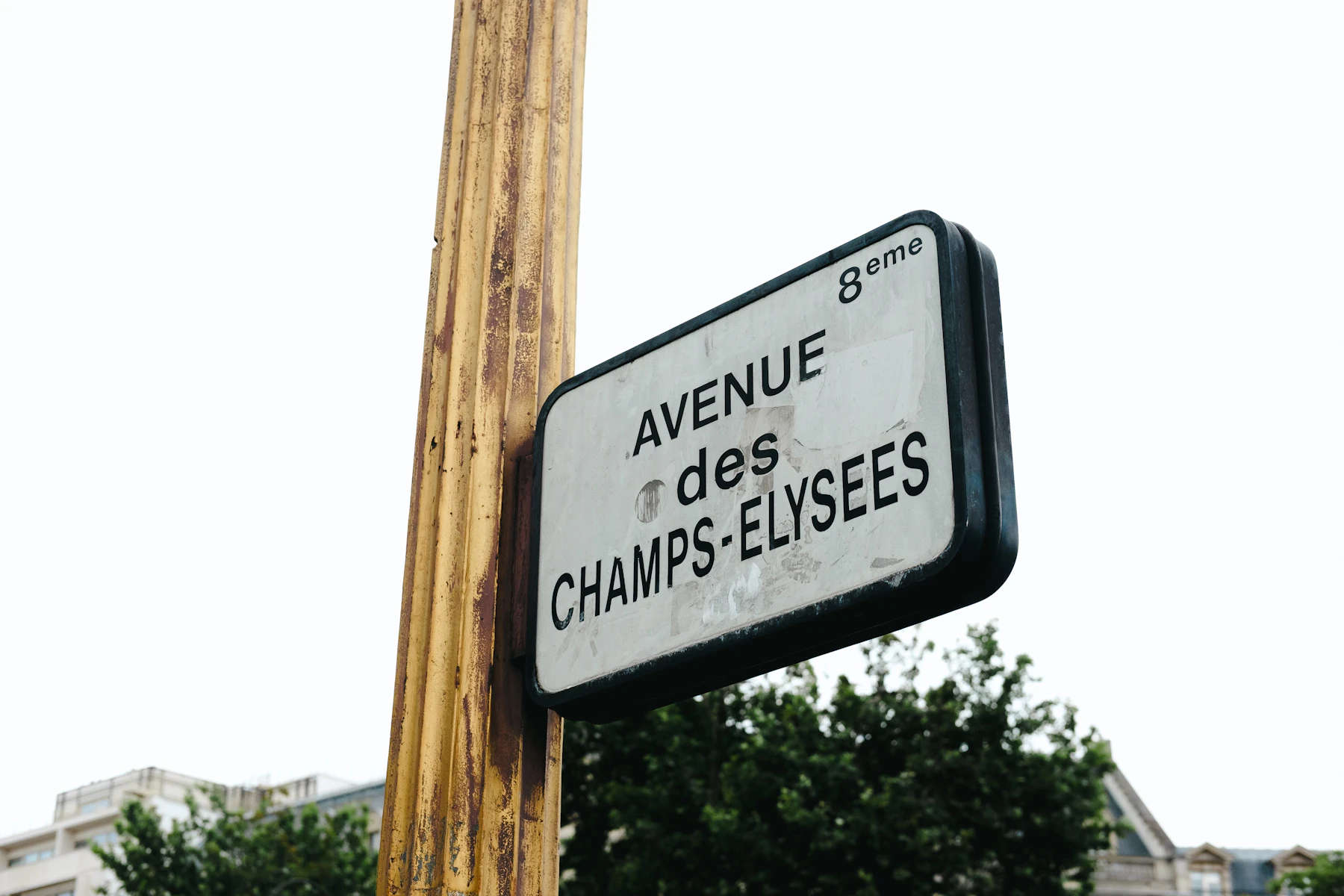 A white Paris street sign on a post, reading Avenue des Champs-Elysees, 8th arrondissement, photographed from below