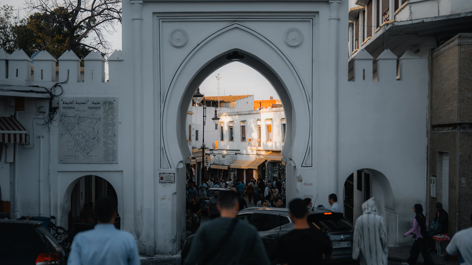 A white arched Moroccan gateway framing a busy street scene in Tangier's medina