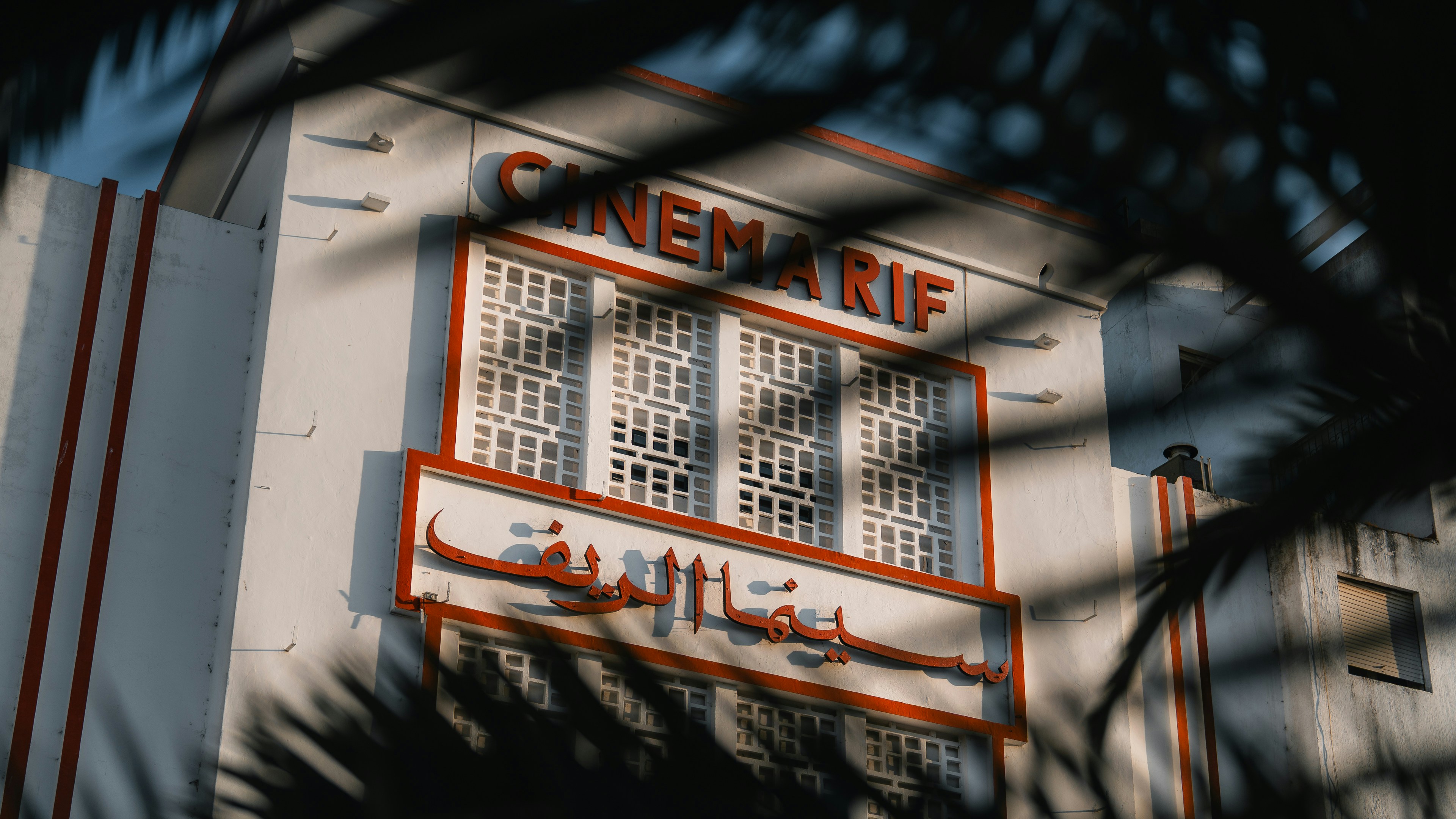 A vintage cinema is framed by palm leaves.