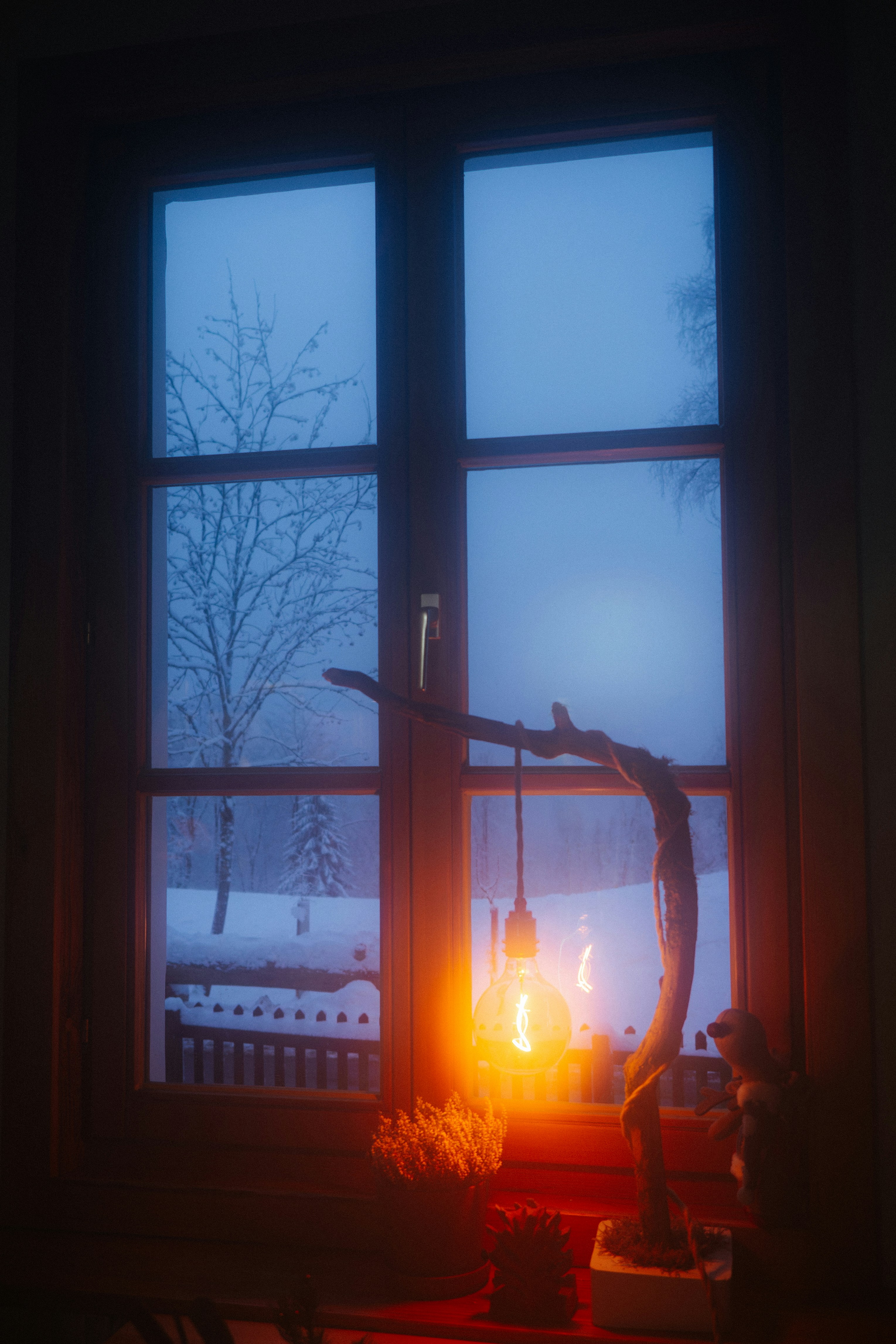 Cozy lamp illuminates a snowy view through the window.