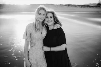 Mother and daughter pose happily on a beach.
