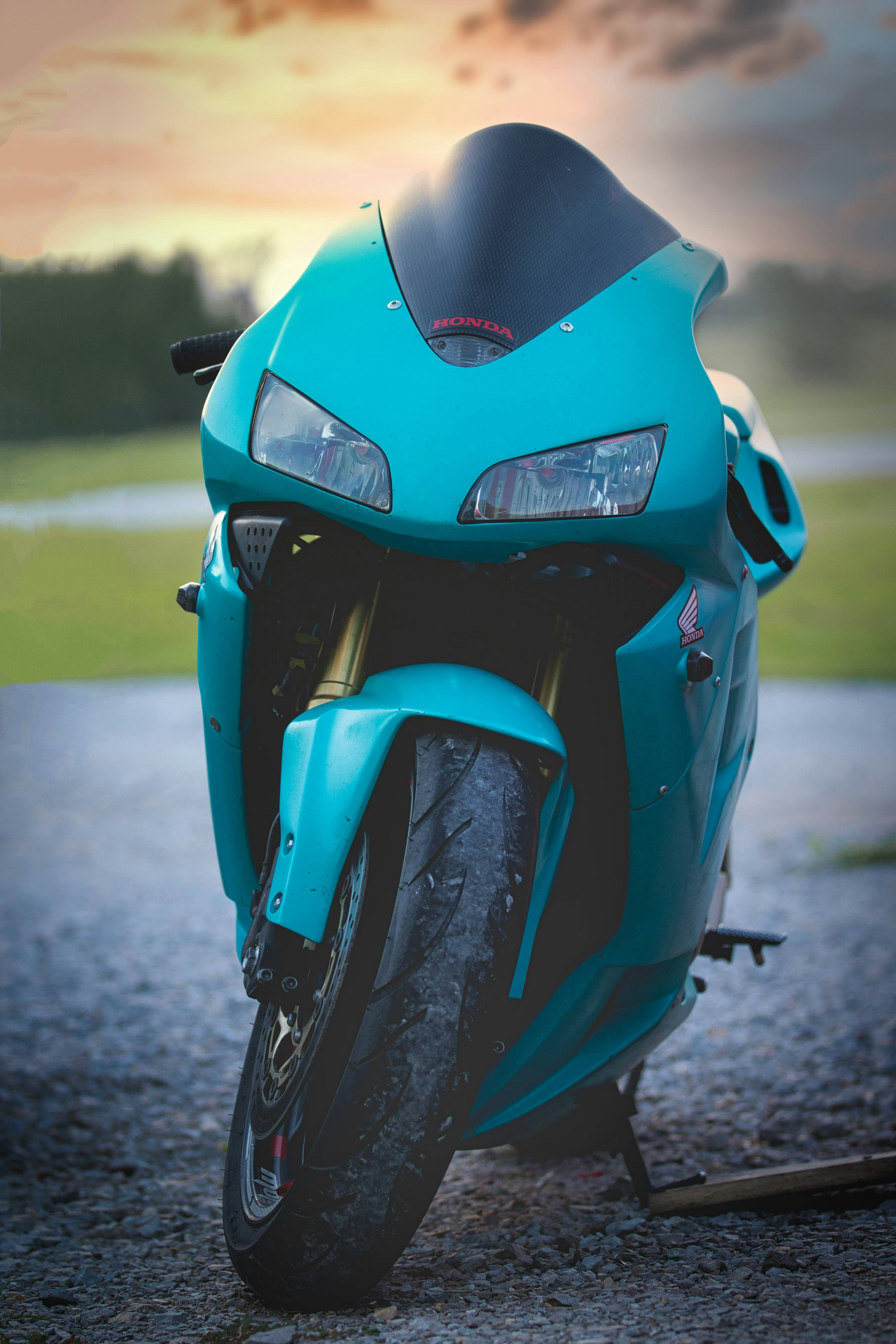 A teal sportbike is parked with an evening sky.