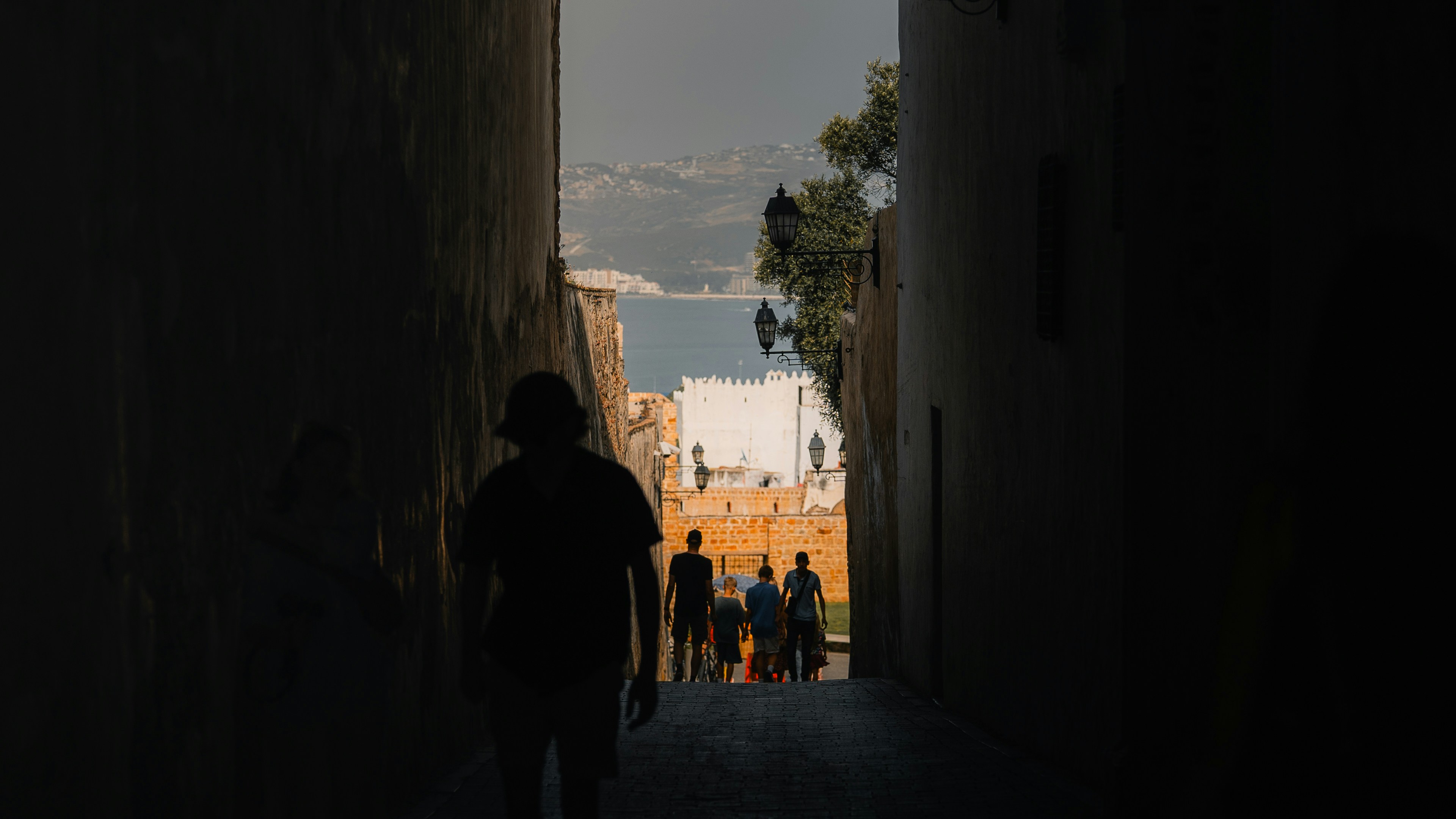 Silhouette walks toward a bright cityscape and water.
