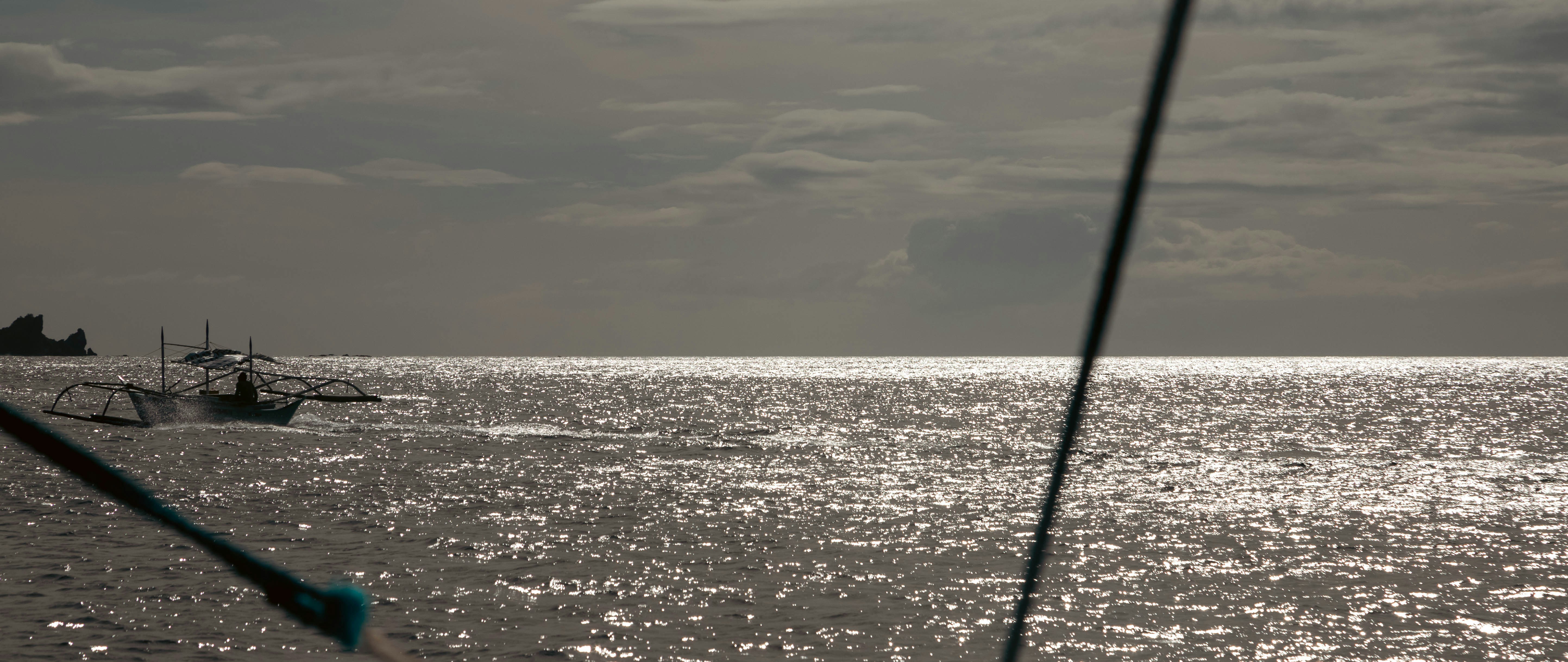 Boats on the shimmering ocean under a cloudy sky.