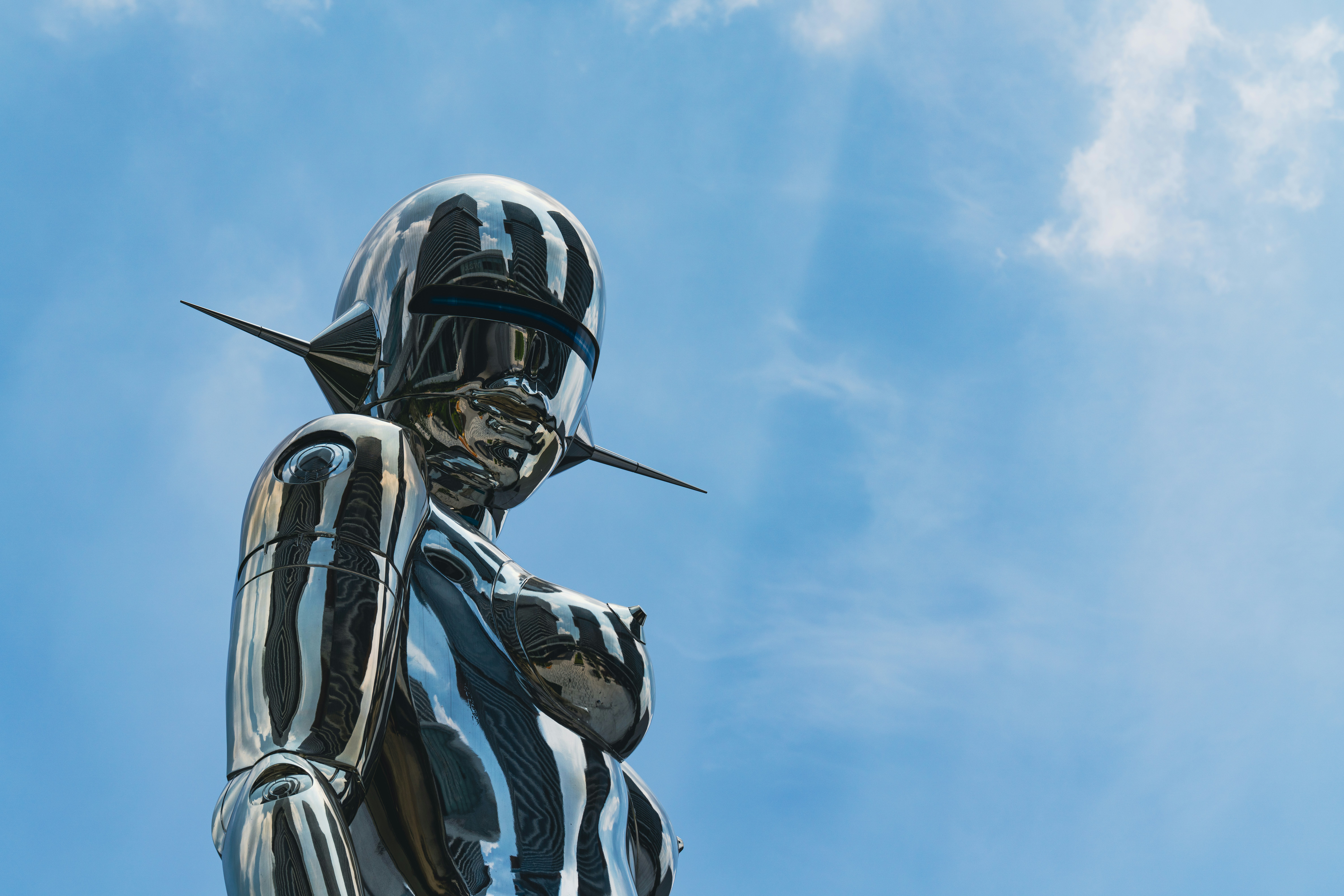 A shiny sculpture stands against a bright blue sky.