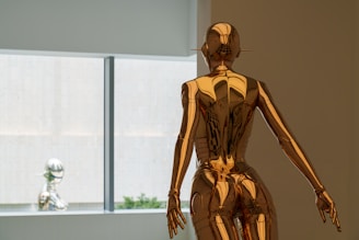 A golden statue stands near a window.