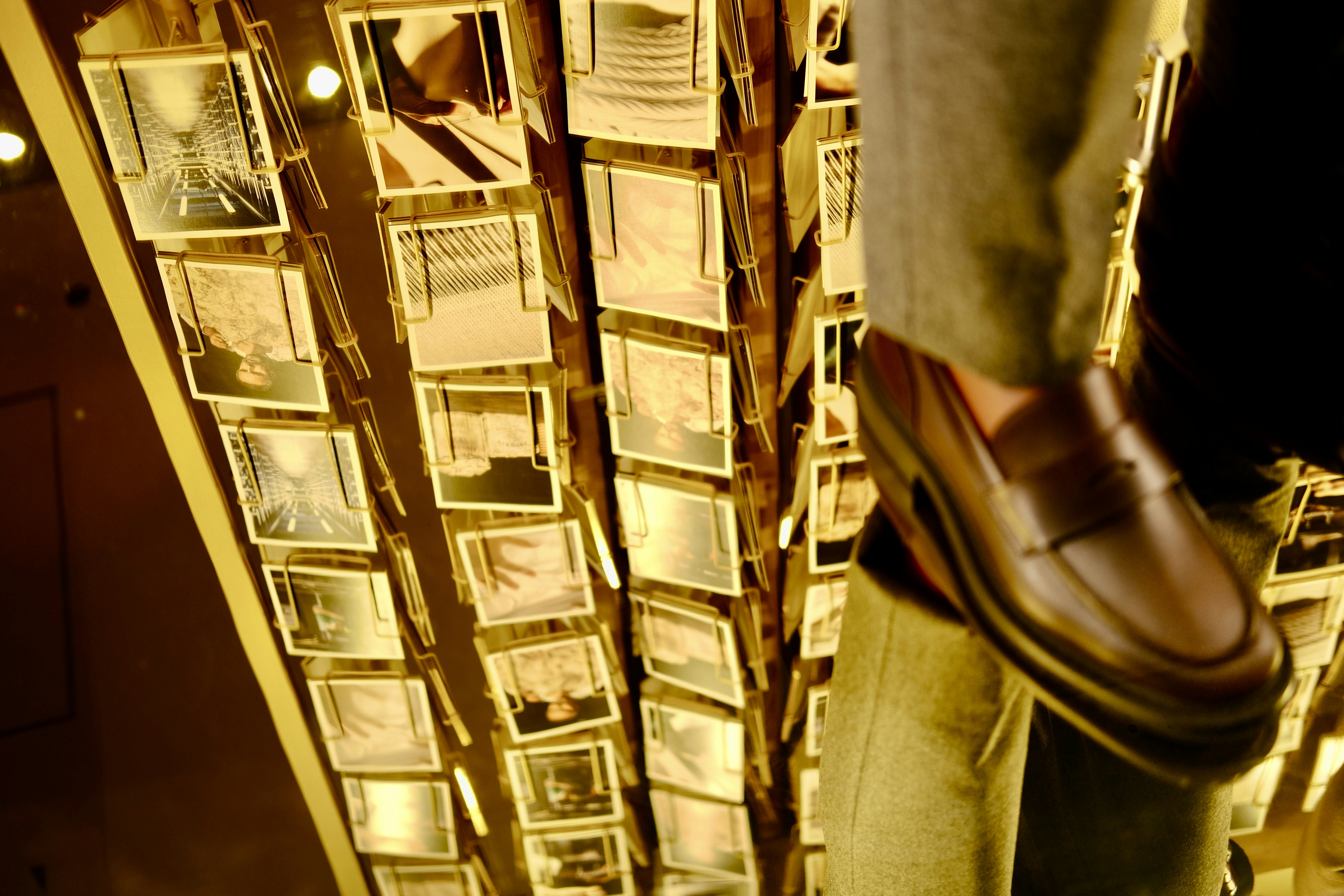 한 남자의 신발이 걸려 있는 사진 옆에 서 있다.