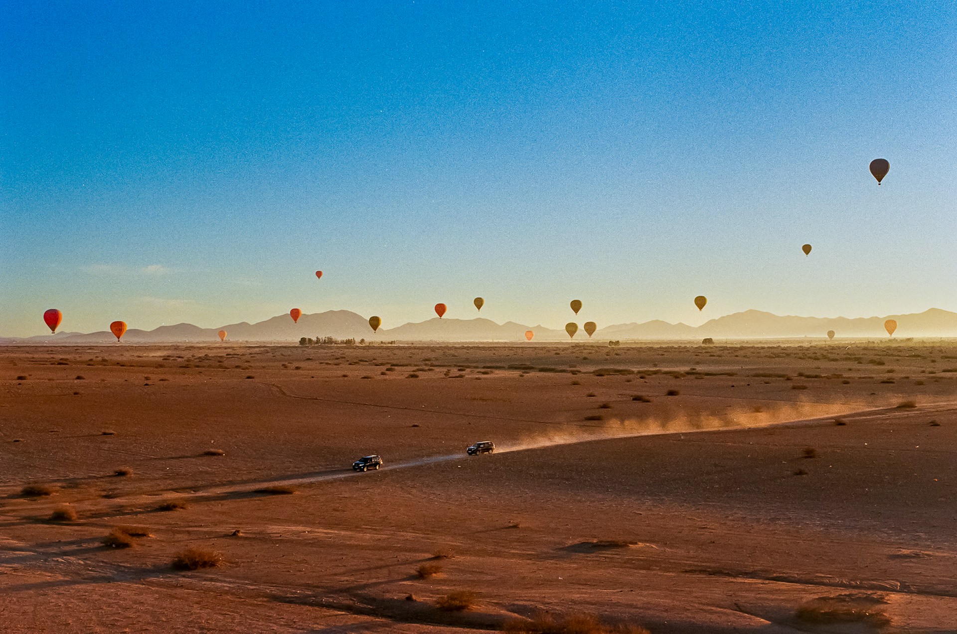 Hot air balloons float above the desert landscape.