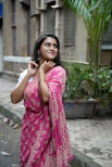 Woman in pink saree smiles outdoors.