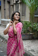 Woman in pink saree smiles outdoors.