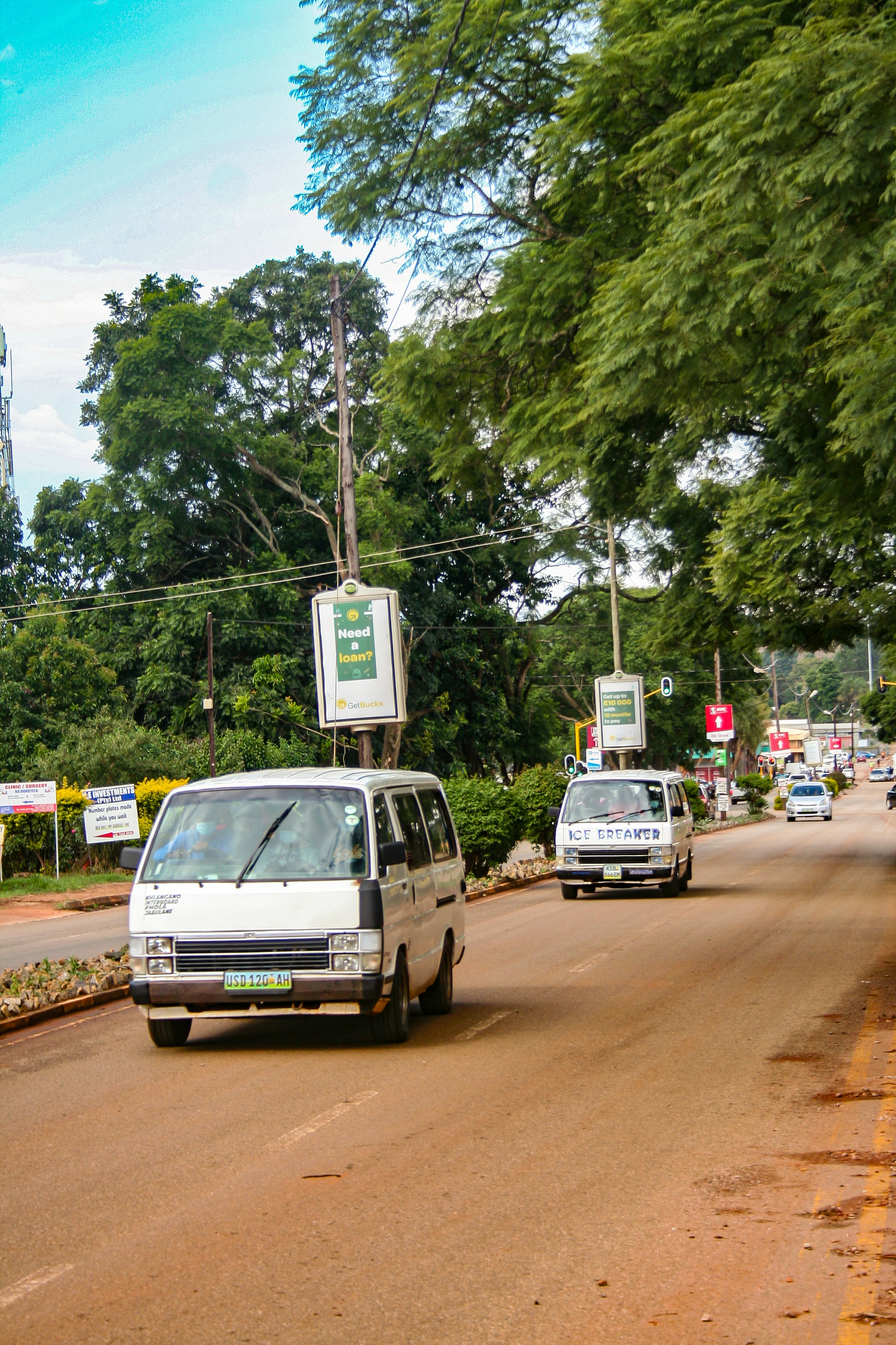 Buses drive down a tree-lined road.