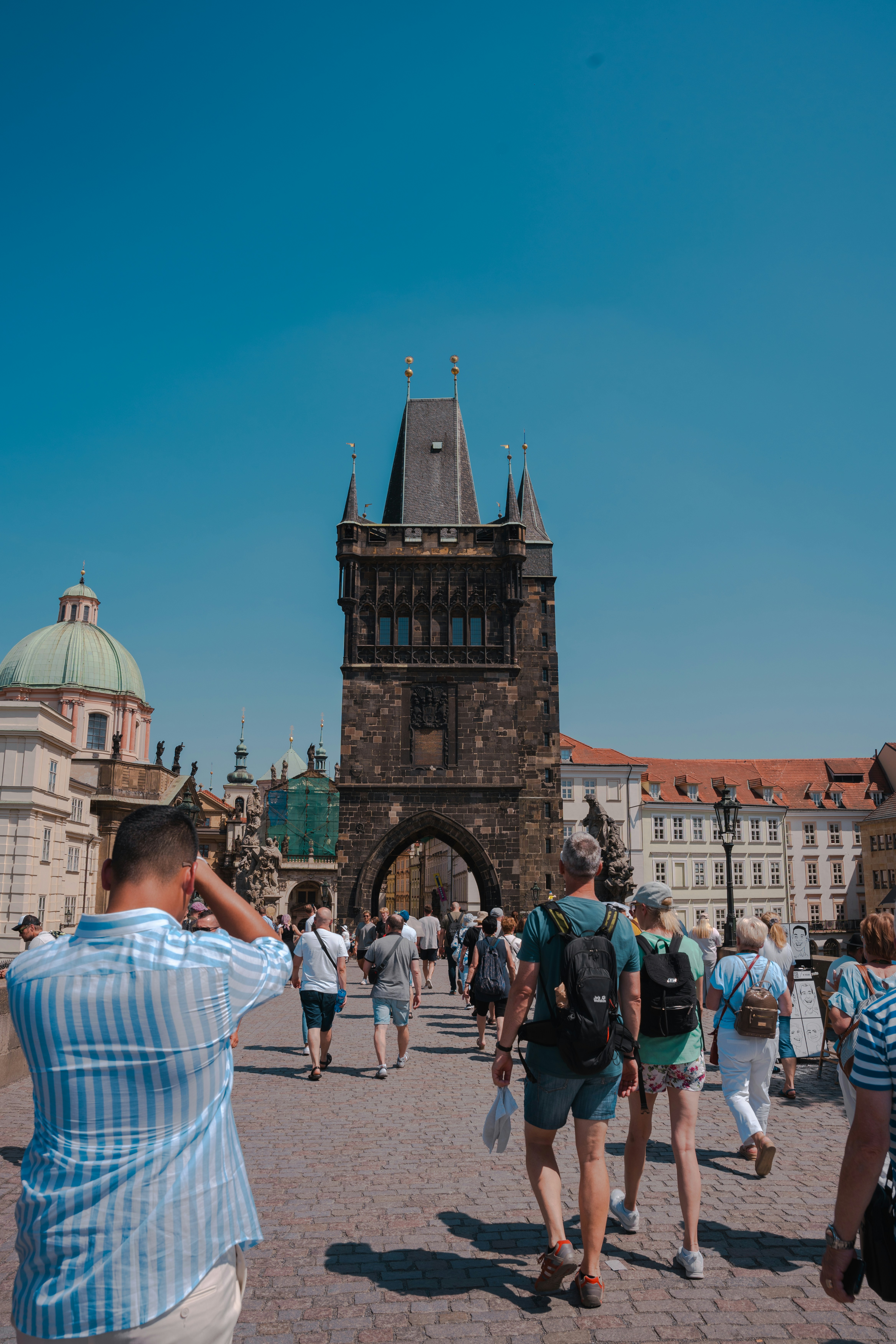 Tourists walk toward a tower under a bright blue sky.