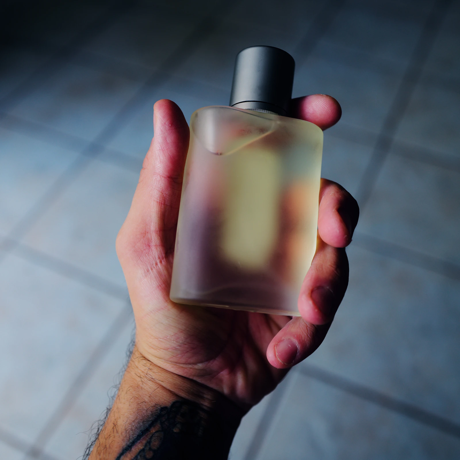 Mão segurando um frasco de perfume diante de um fundo lilás