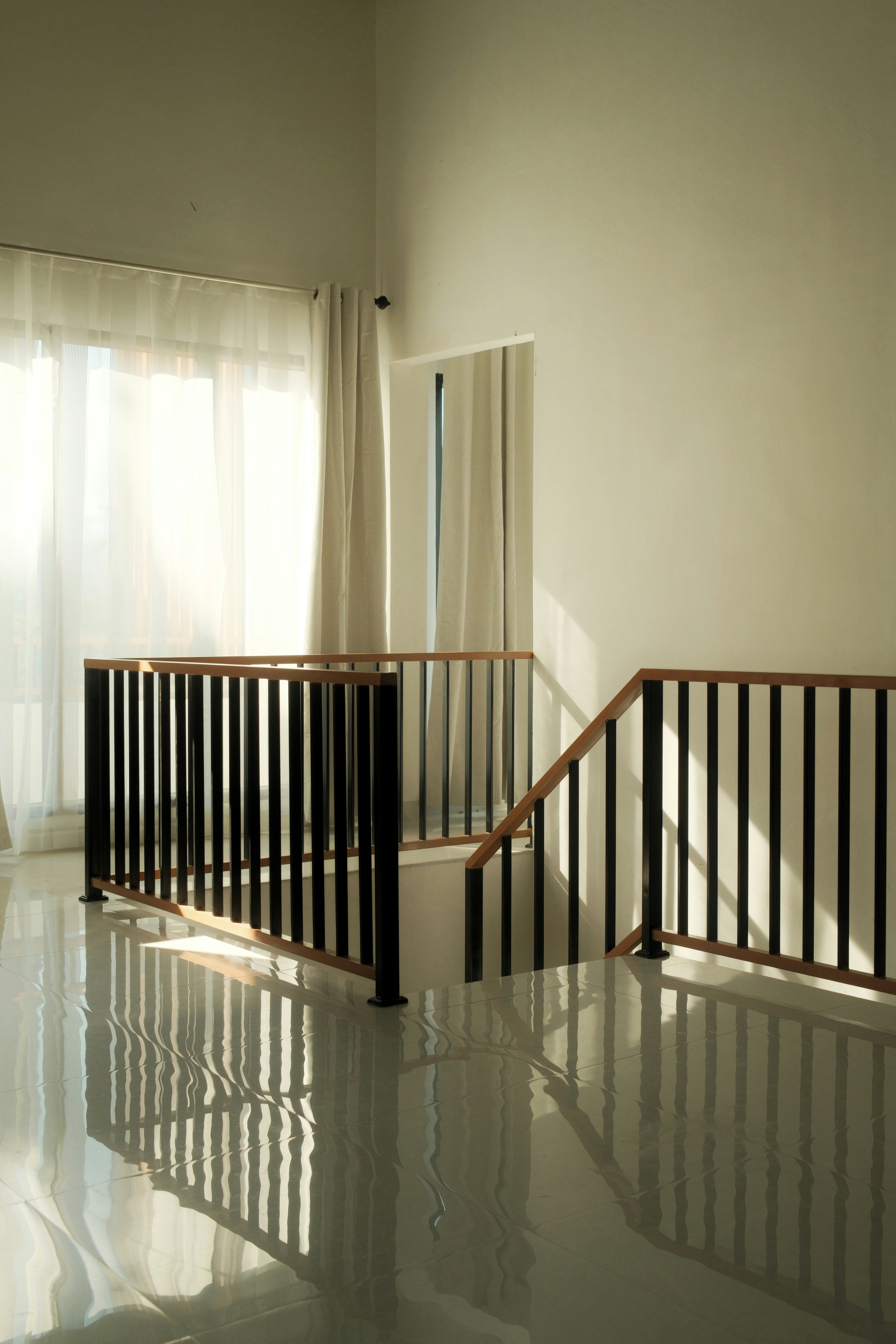 Stairway railing reflects on a shiny white floor.