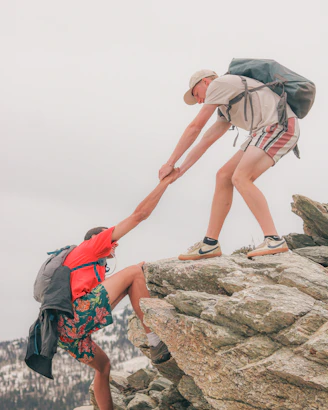Two hikers help each other climb a rocky terrain
