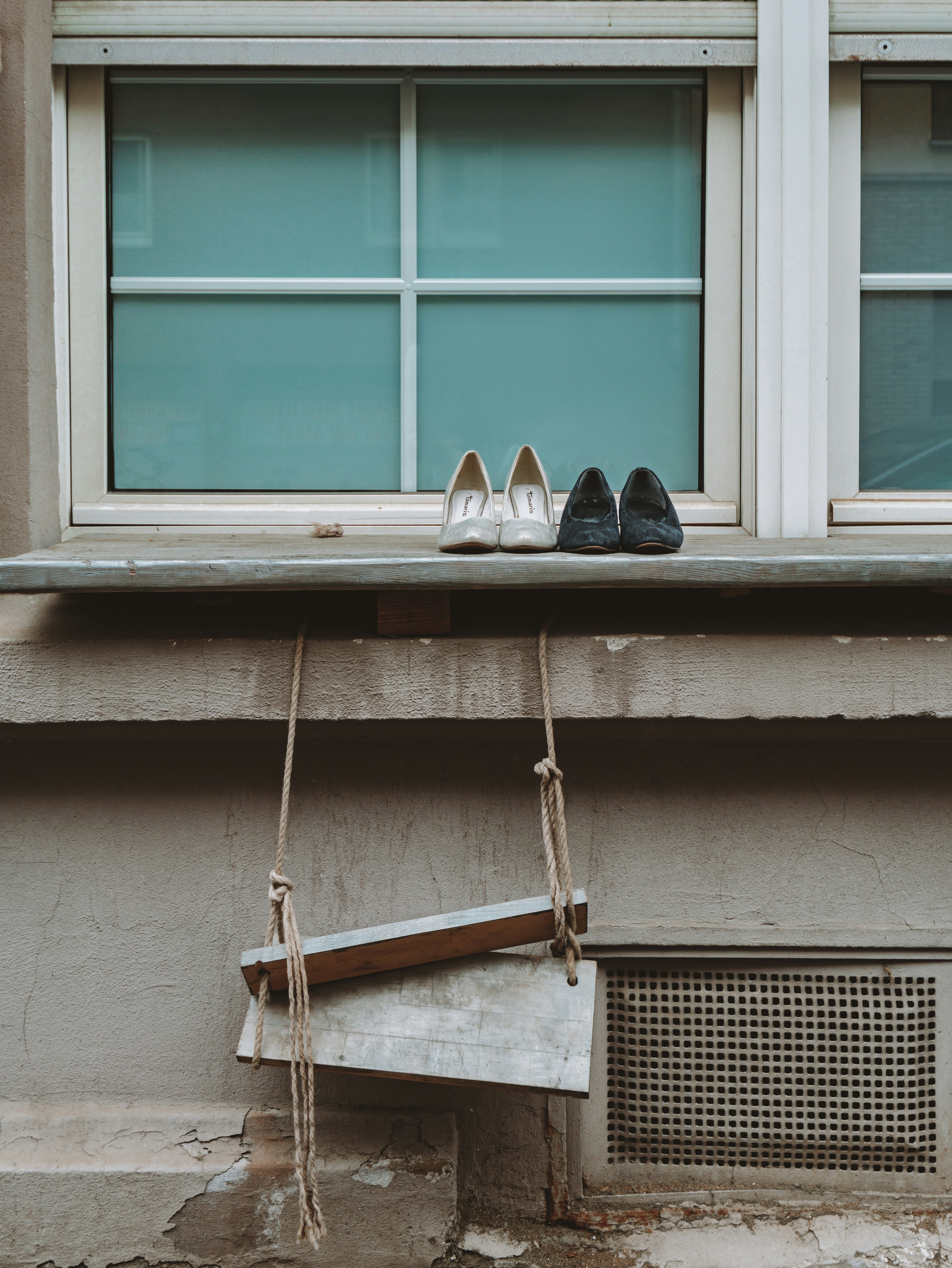 Shoes sit on a windowsill above a small swing.