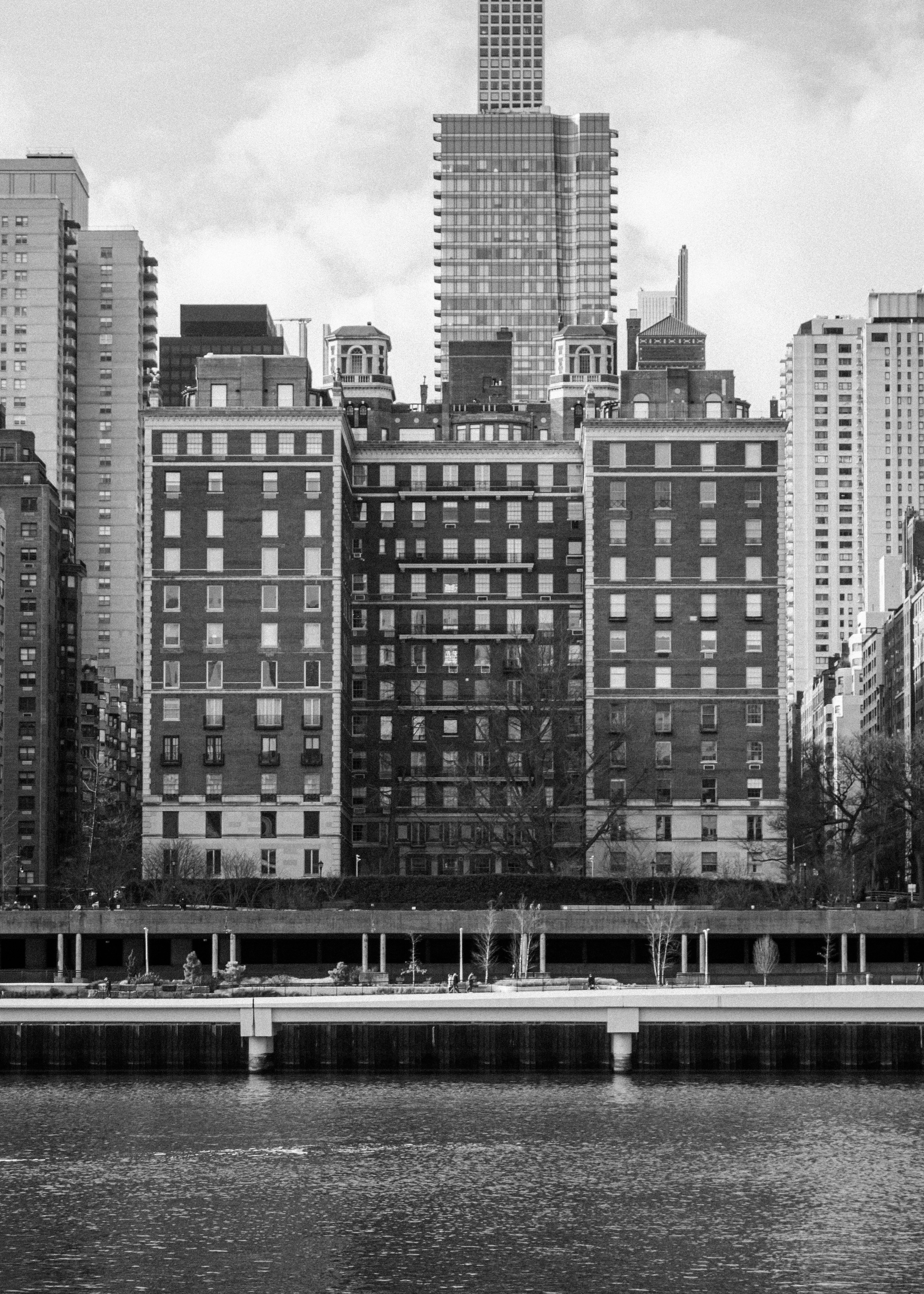 A view of One Sutton Place South, a 14-story, 42-unit cooperative apartment building in Manhattan, New York City. It overlooks the East River and is located between 56th and 57th Streets. The building is known for its elegant architecture and has been home to diplomats, industry leaders, and media executives. It was designed by Rosario Candela and built in 1927. The building features a triple-arched entrance driveway and gardens. The area is considered a quiet and upscale neighborhood with views of the East River.