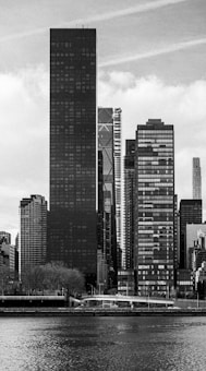 Skyscrapers line a river in this black and white image.