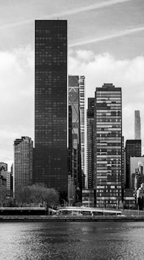 Skyscrapers line a river in this black and white image.