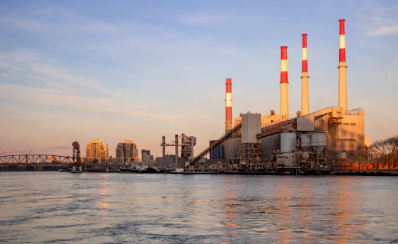 A power plant stands near water under a blue sky