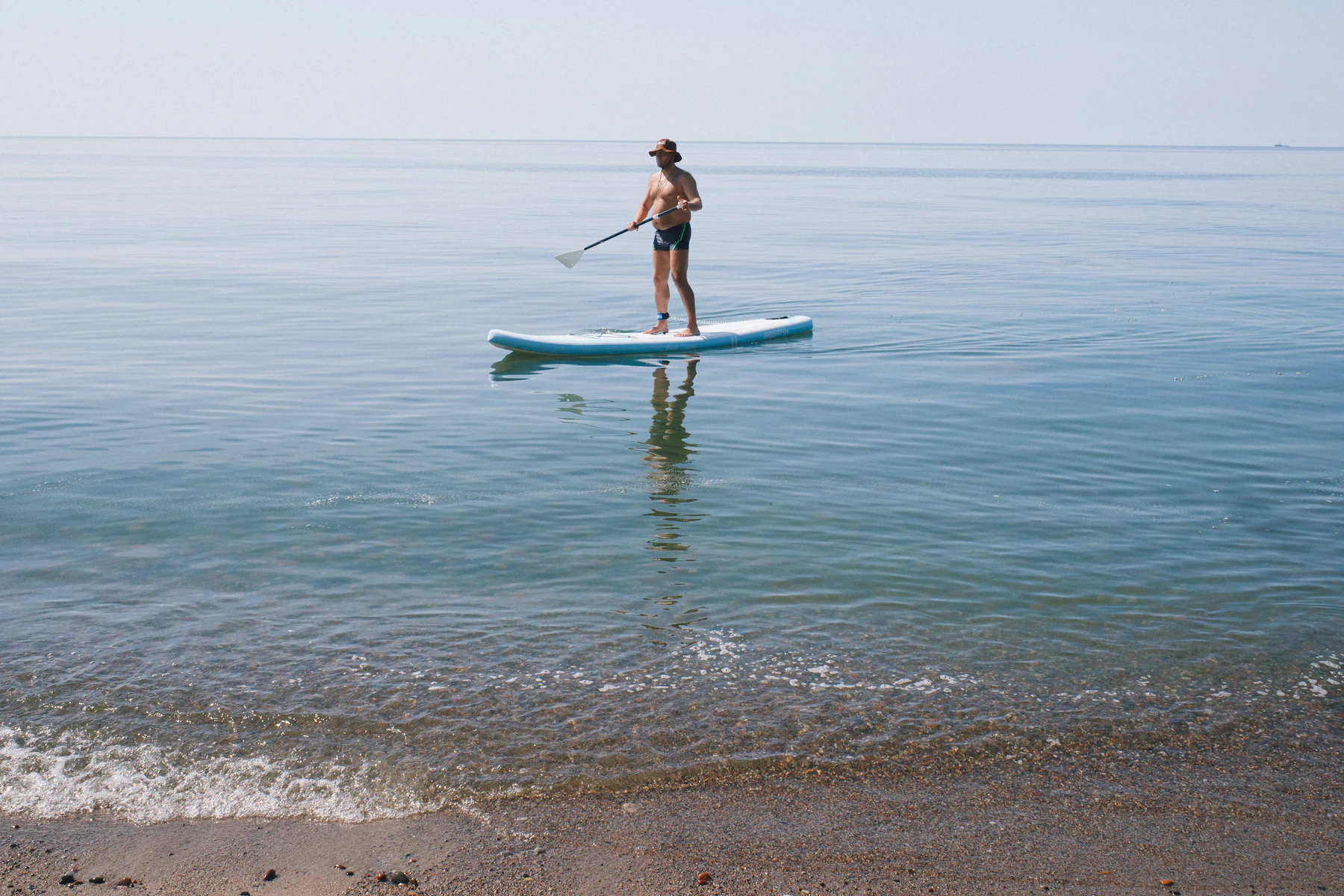 Paddleboarder moving across calm open water with a paddle