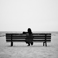 A person sits alone on a beach bench.
