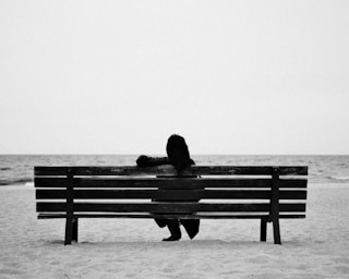 A person sits alone on a beach bench. by Kirill Shavlo (@svl_photo)