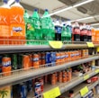 Soda bottles and cans are stocked on supermarket shelves.