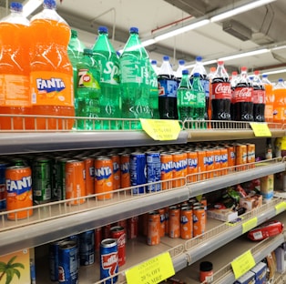 Soda bottles and cans are stocked on supermarket shelves.