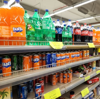 Soda bottles and cans are stocked on supermarket shelves.