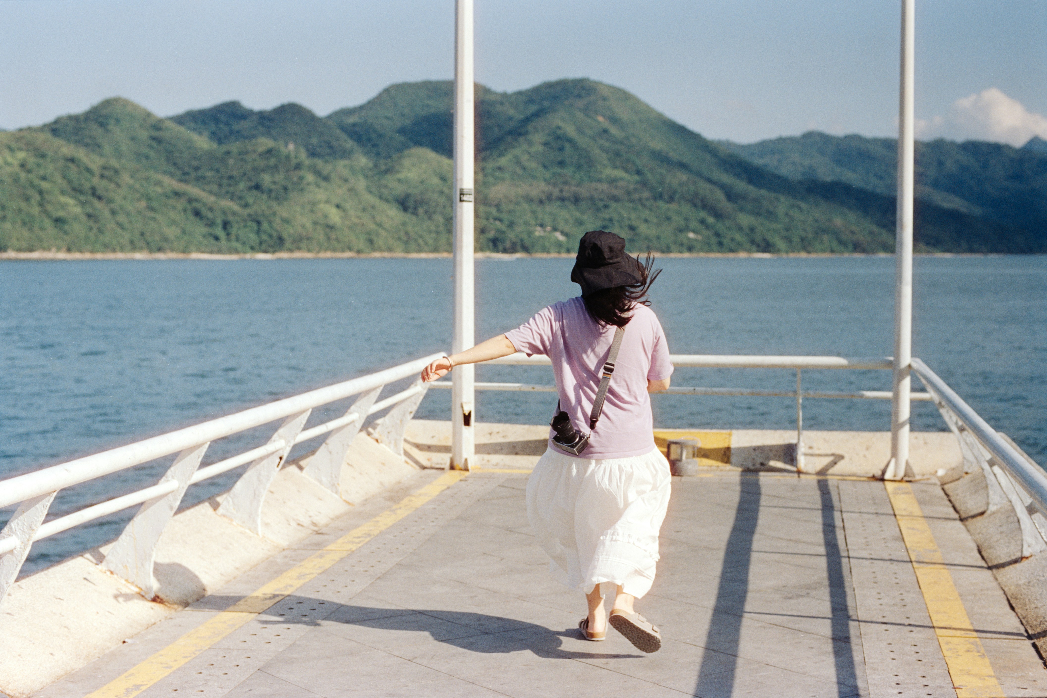 A woman walks on a pier toward the mountains.