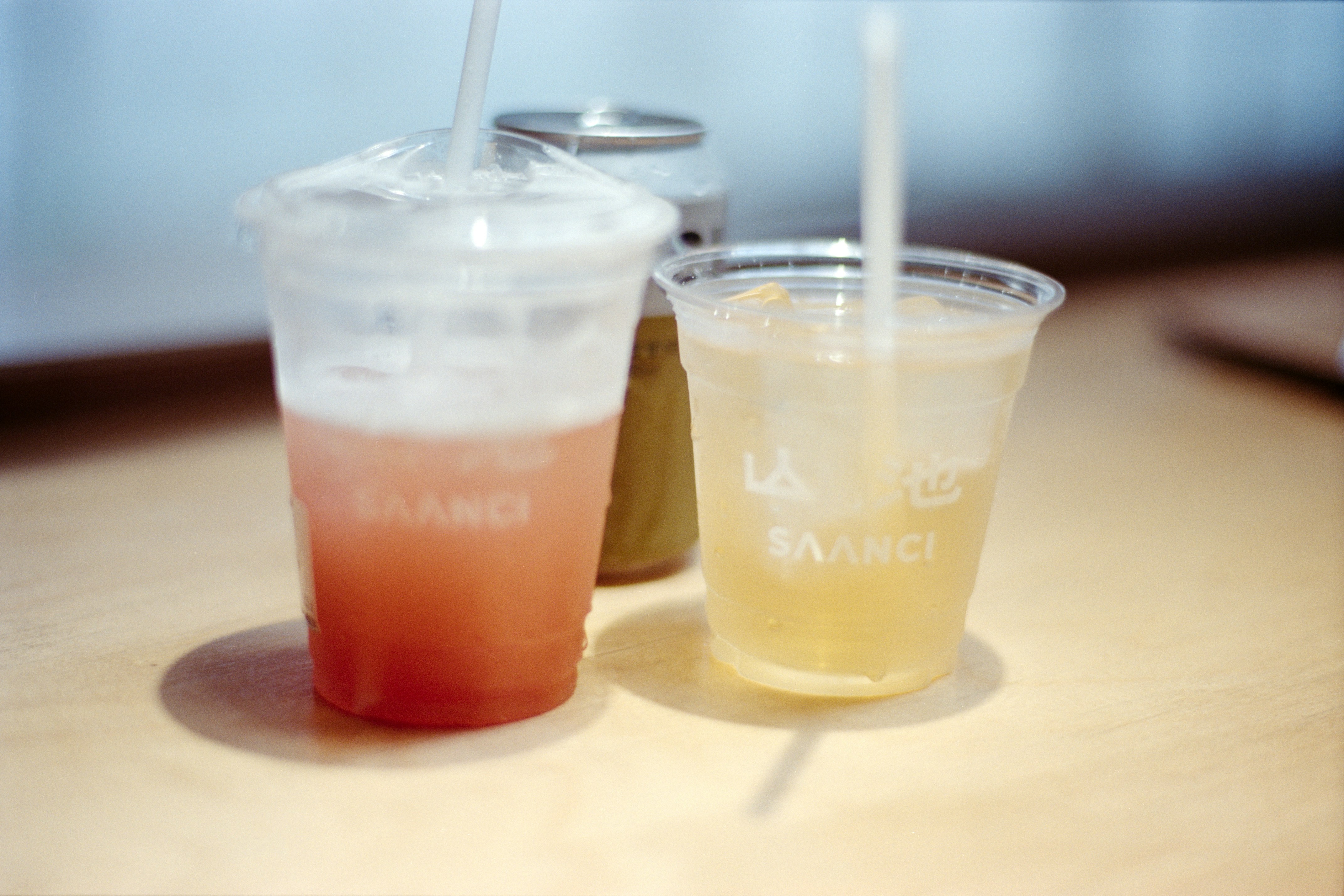 Two colorful drinks with straws and a small can.