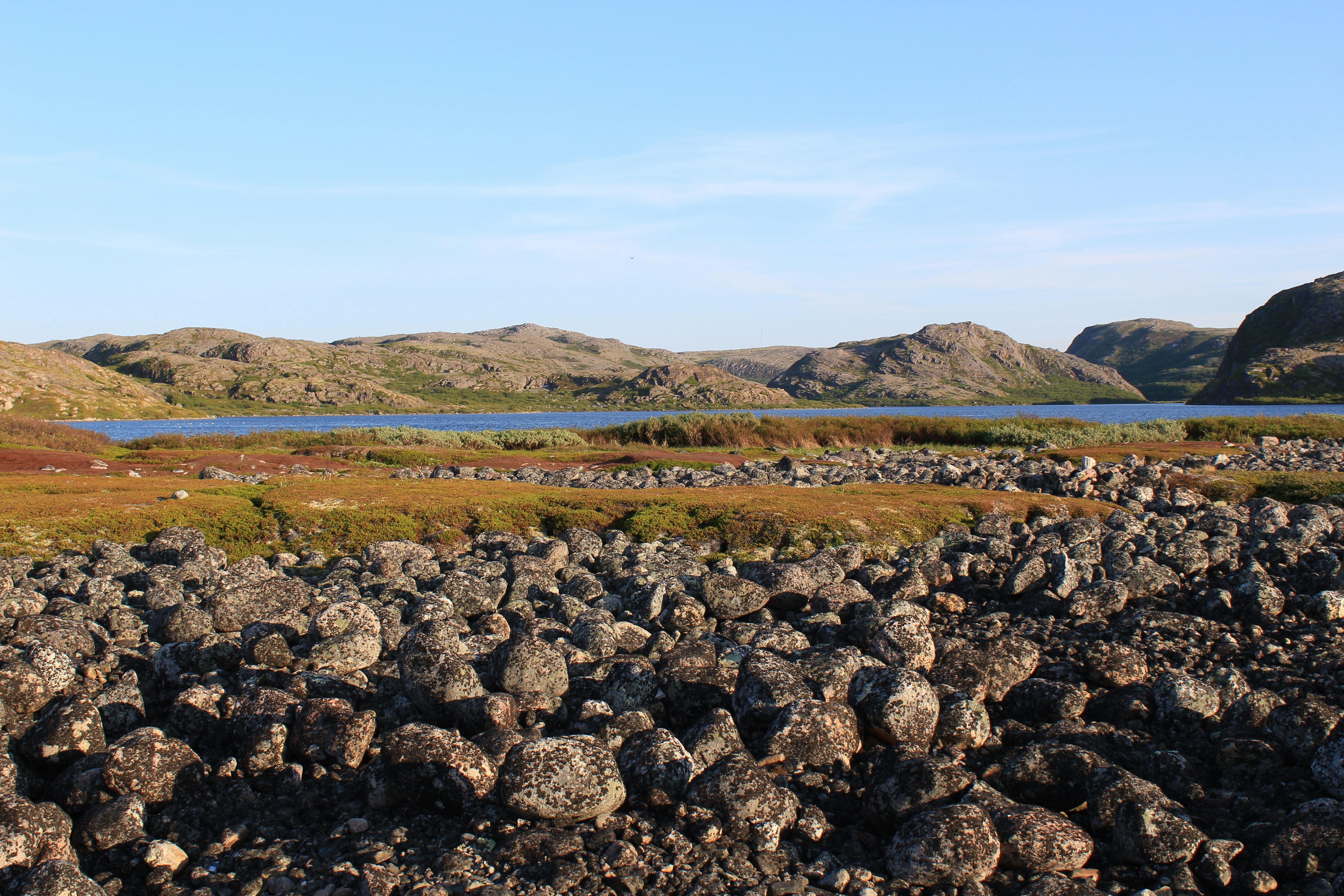 Rocky landscape with lake and hills under blue sky.