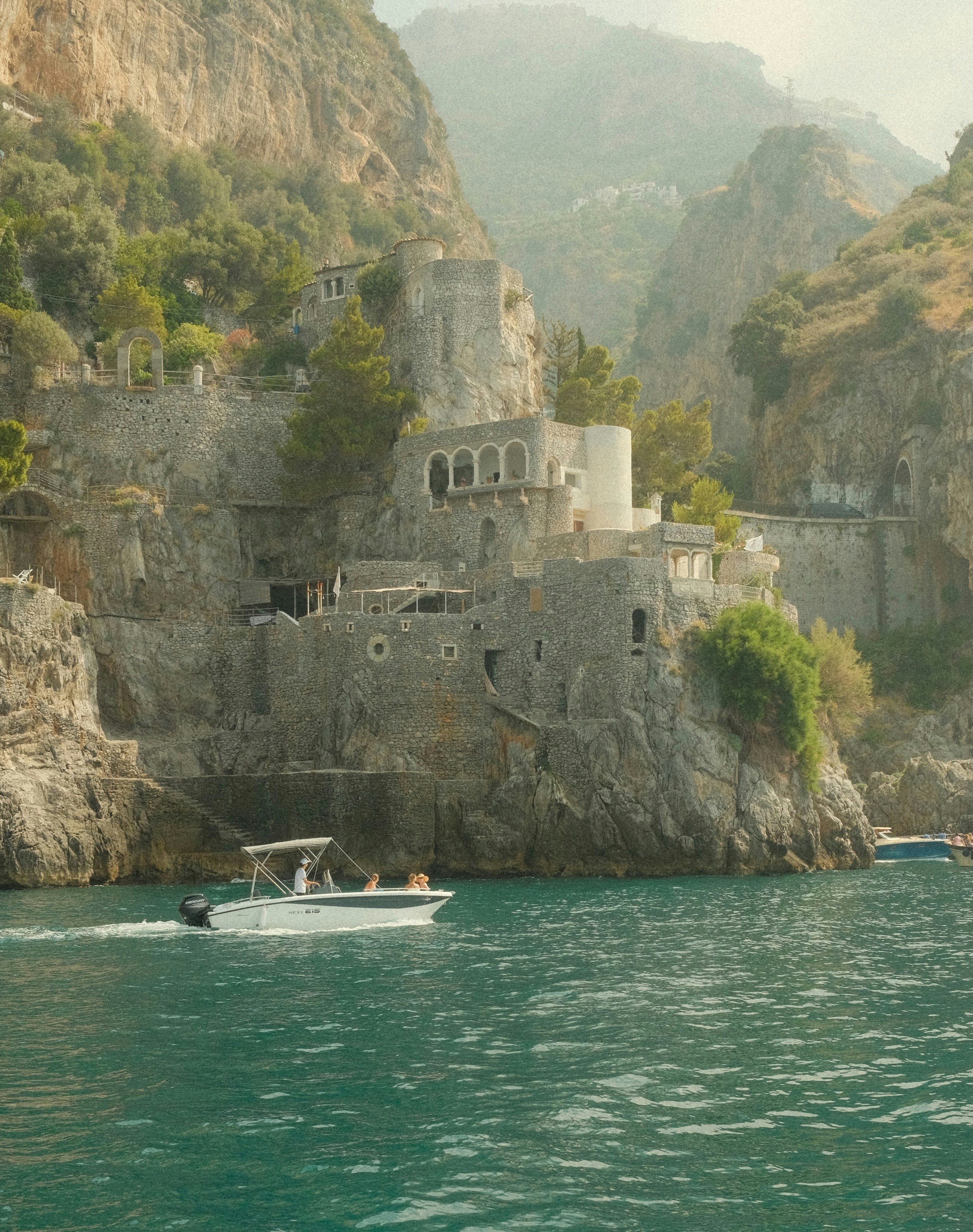 A boat cruises near a cliffside castle.