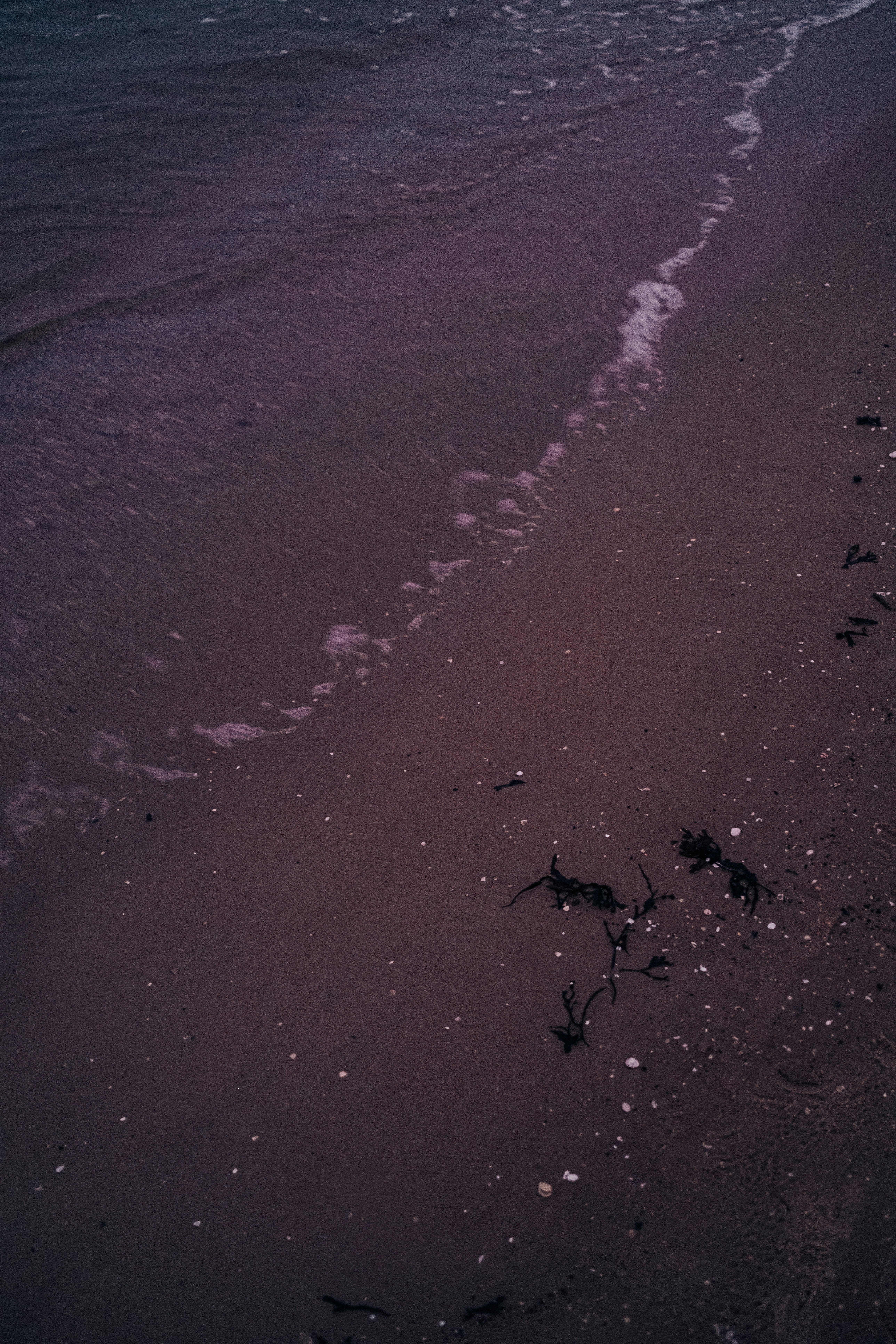 Waves gently lap on a dark, sandy beach.