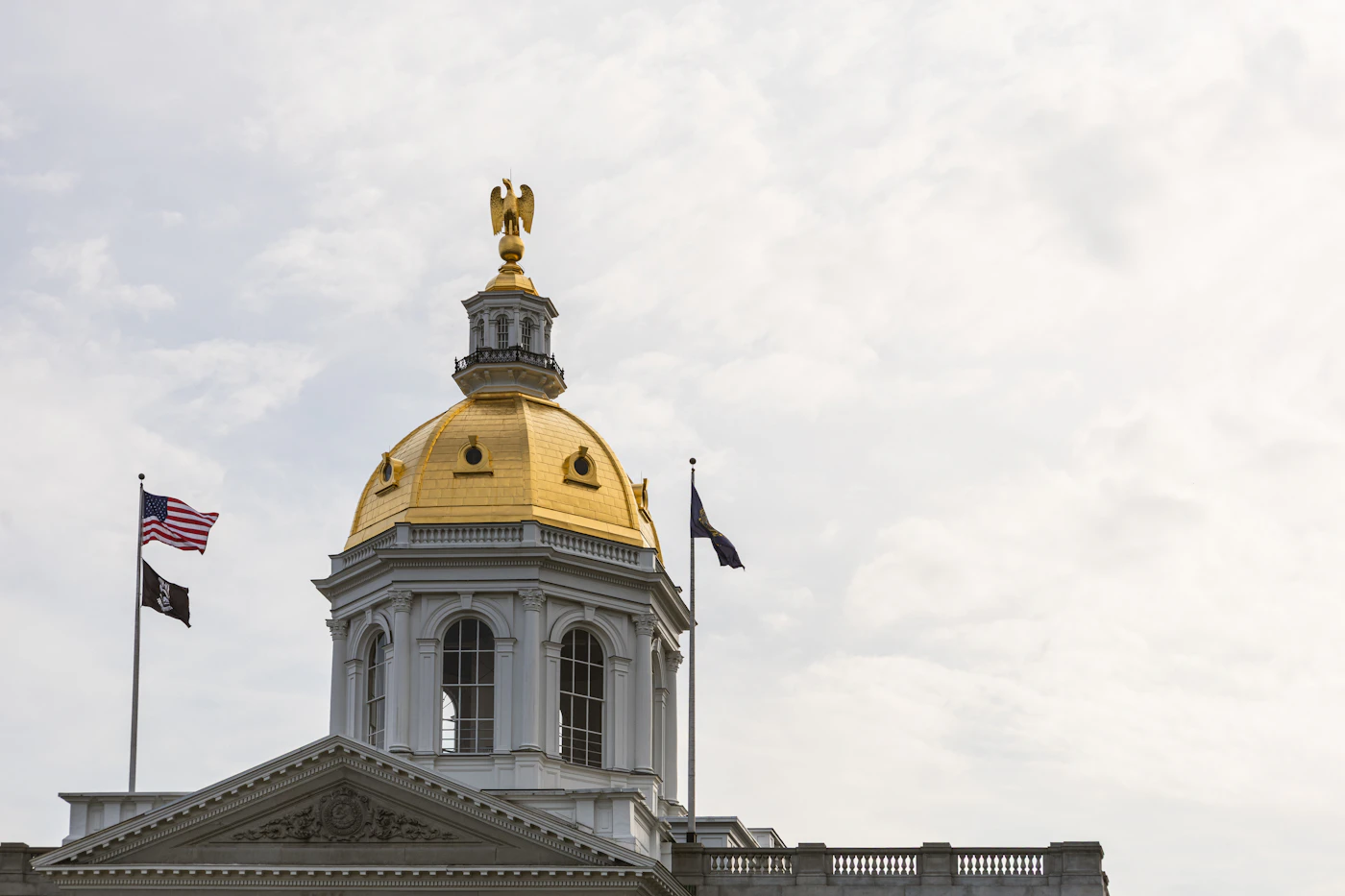 The gold dome and eagle of the New Hampshire State House with flags flying, the destination for many people booking a car rental in Concord, NH