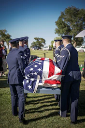 Military officers carry a casket draped in the american flag.