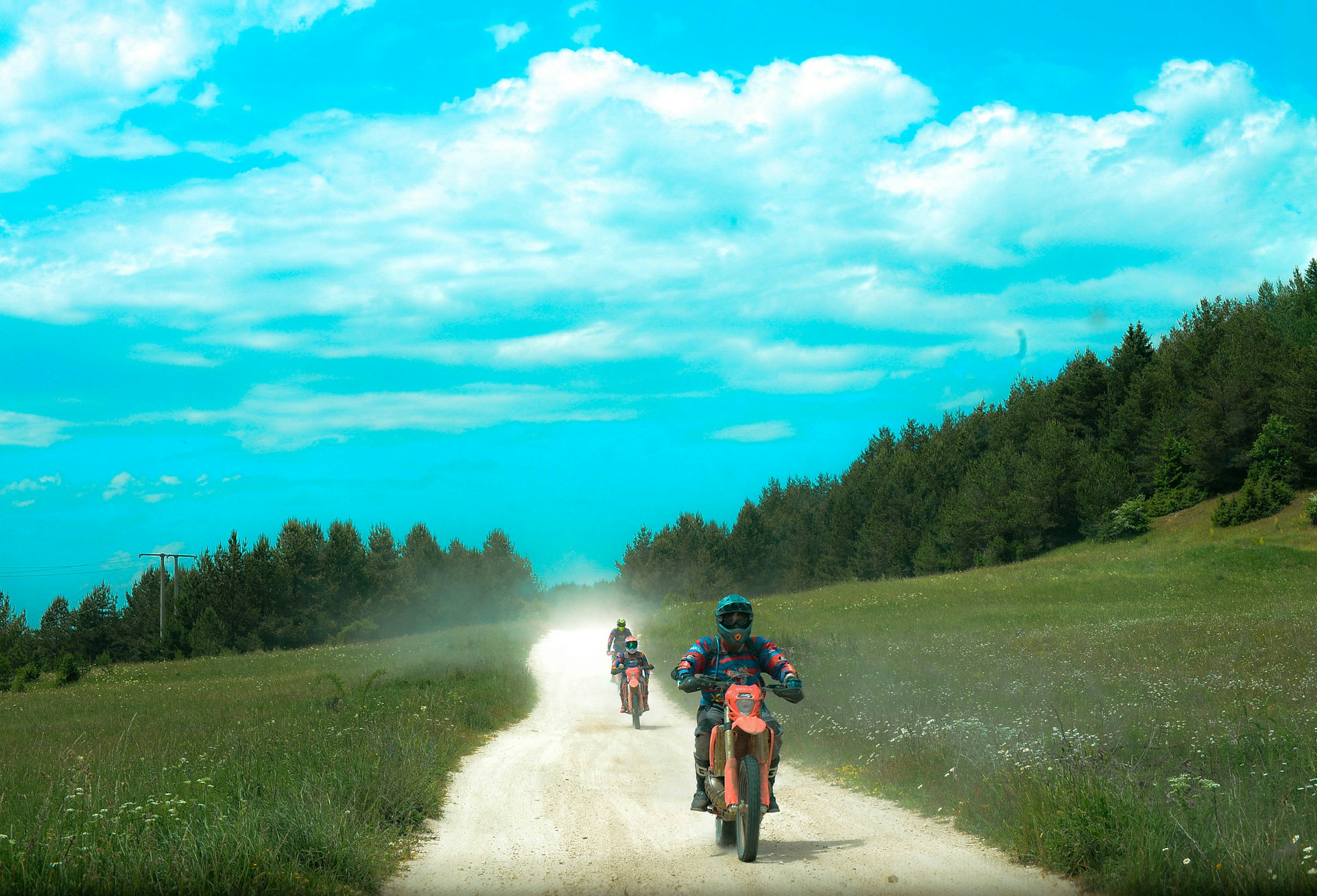 Motorcyclists ride down a dusty road in nature.