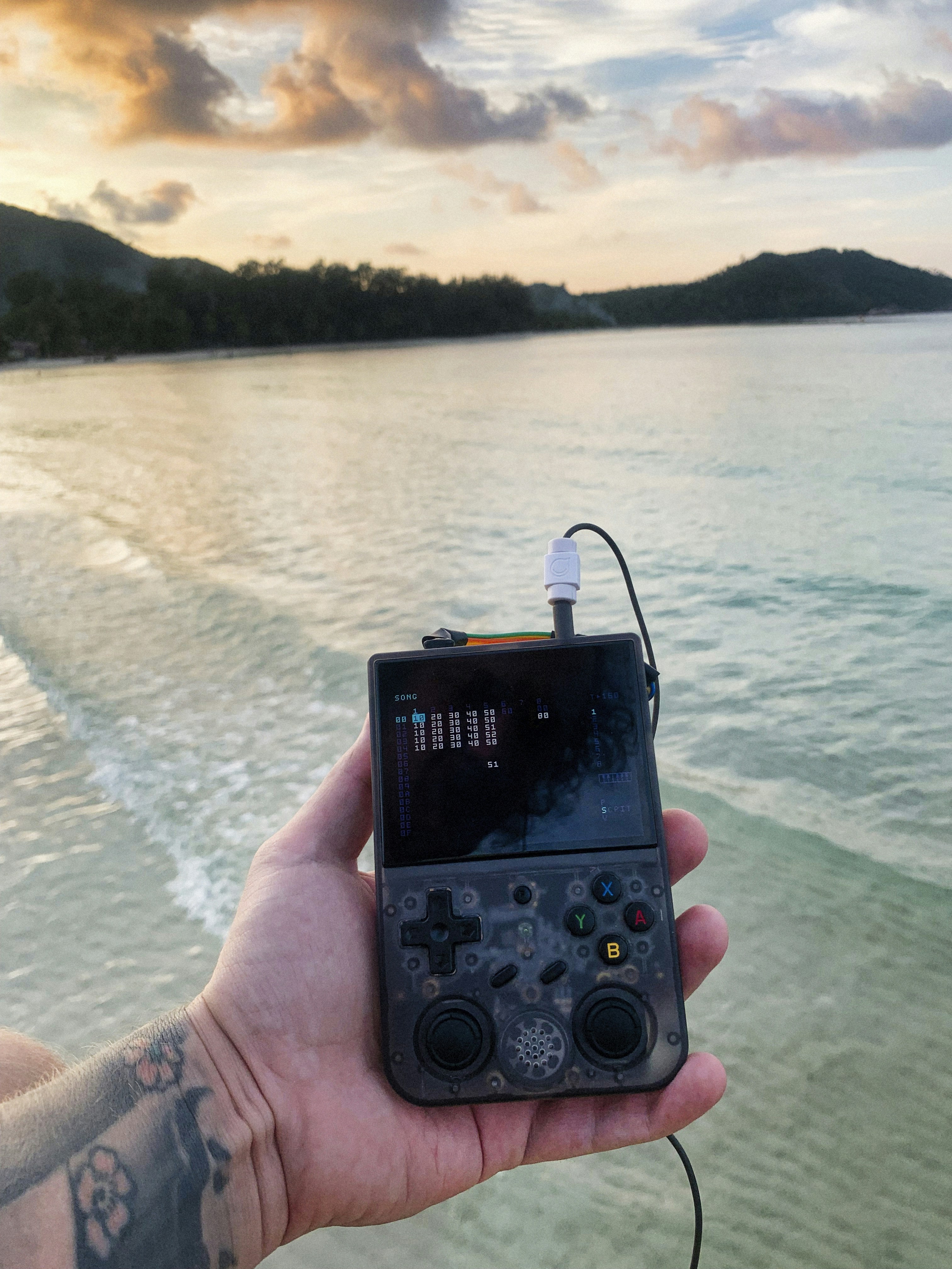 Hand holding a gaming console by the ocean