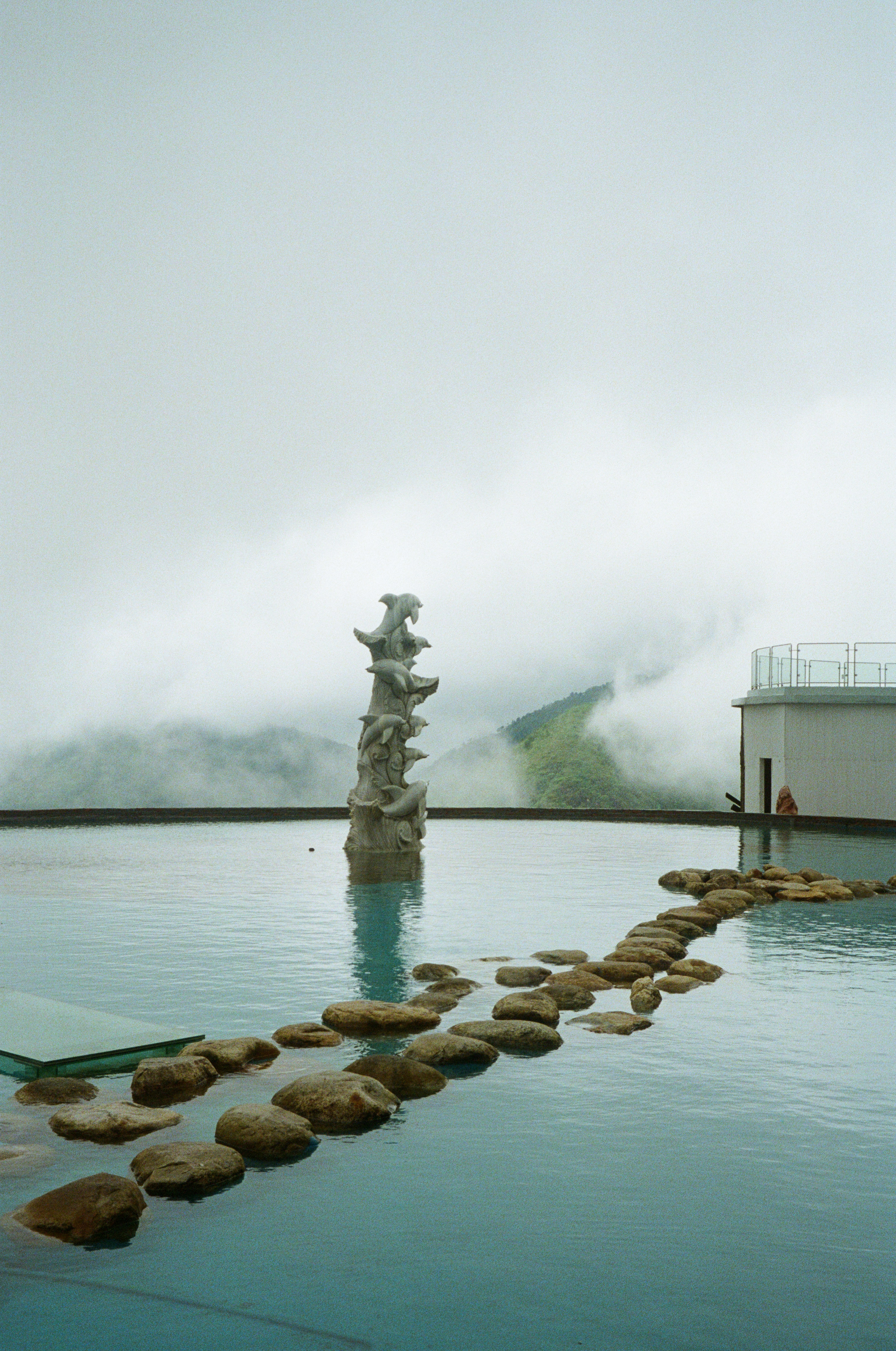Stone pathway leads to sculpture in water.