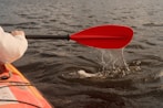 Kayaking through the water with a red paddle.