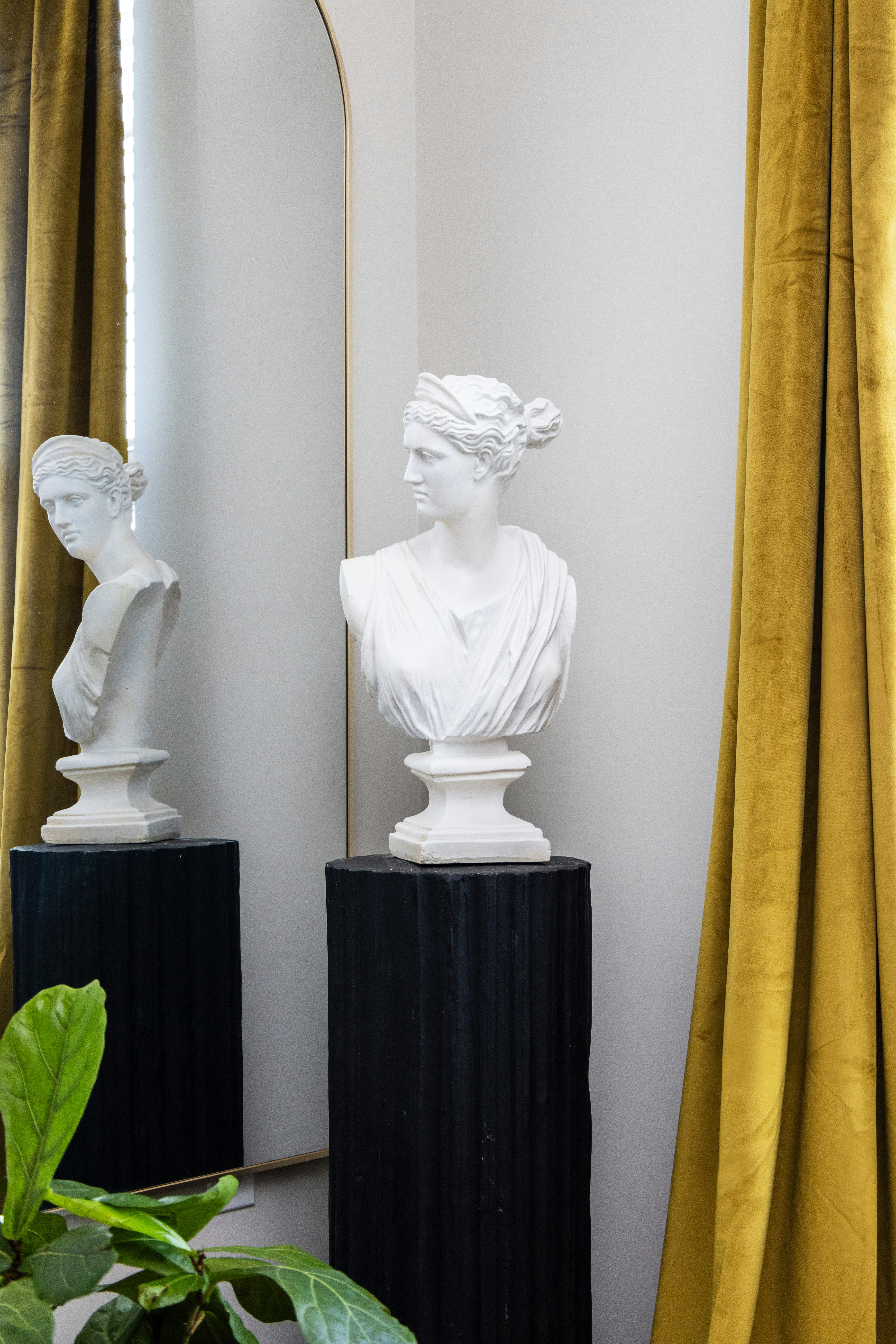 A statue bust stands next to a mirror and curtain.