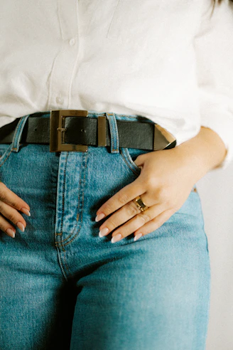 Person wears a belt and jeans with hand in the pocket.