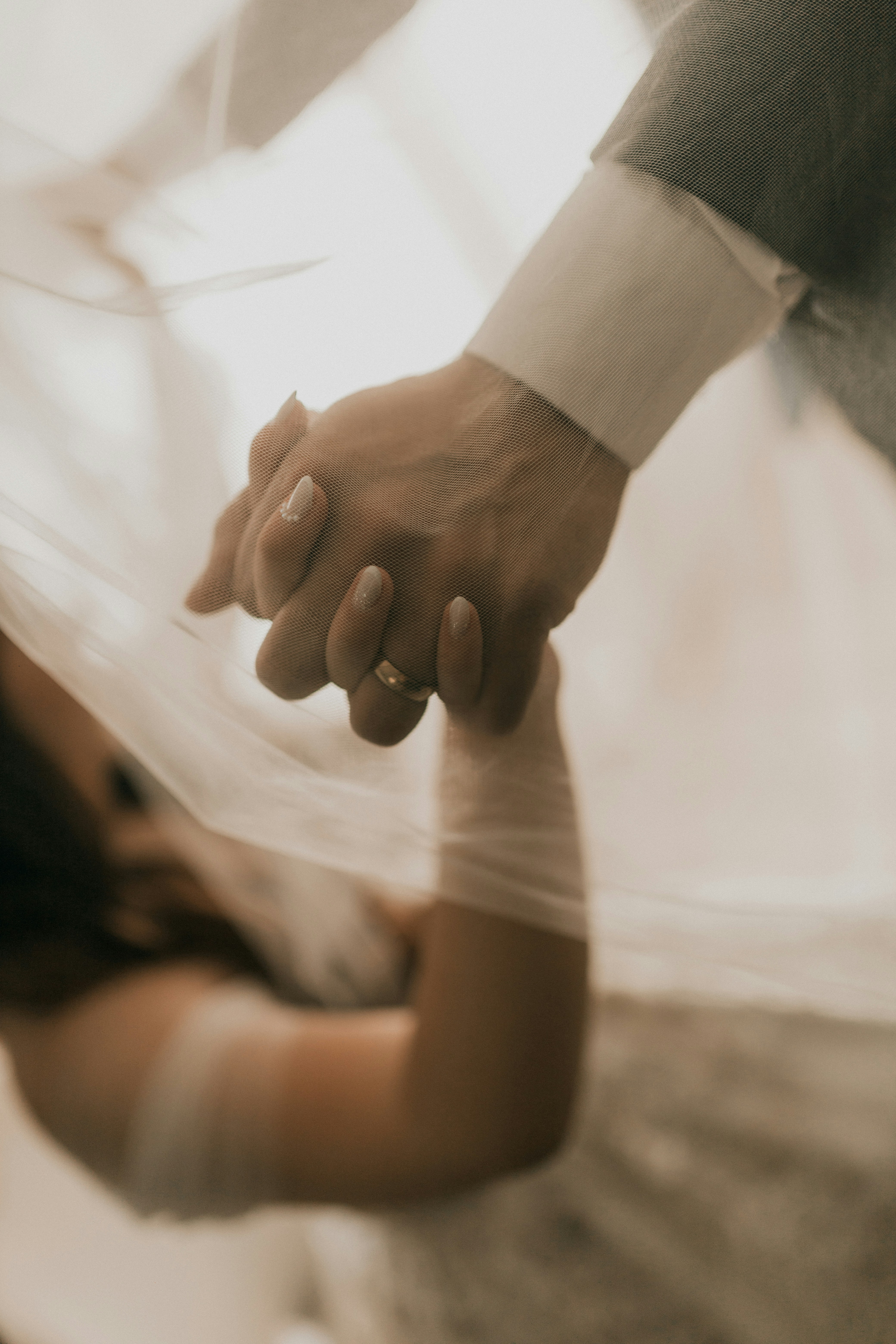Pengantin berpegangan tangan di bawah kerudung.